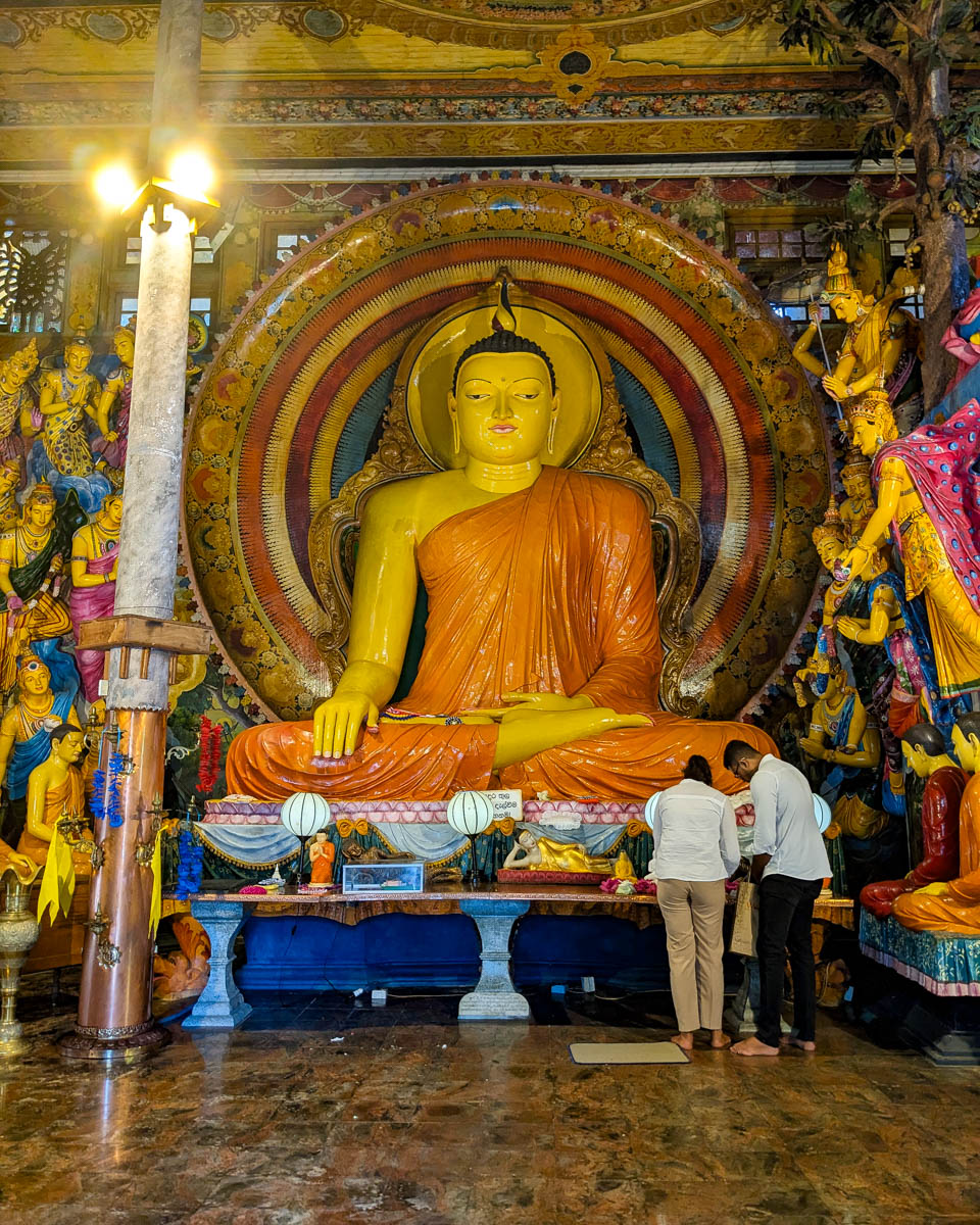 Two Sri Lankan people make an offering to a large Buddha at the shrine of Gangarama temple Colombo, Sri Lanka