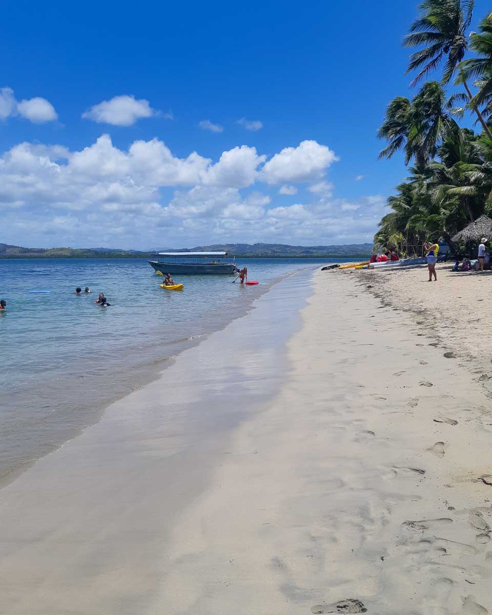 Visitors to robinson crusoe island on the beach swimming with boats in the background fiji