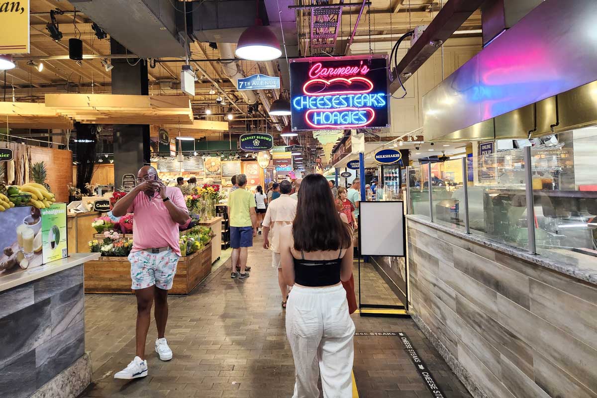 A woman walking through Reading Terminal Market Philadelphia with a sign that says chesters hoagies