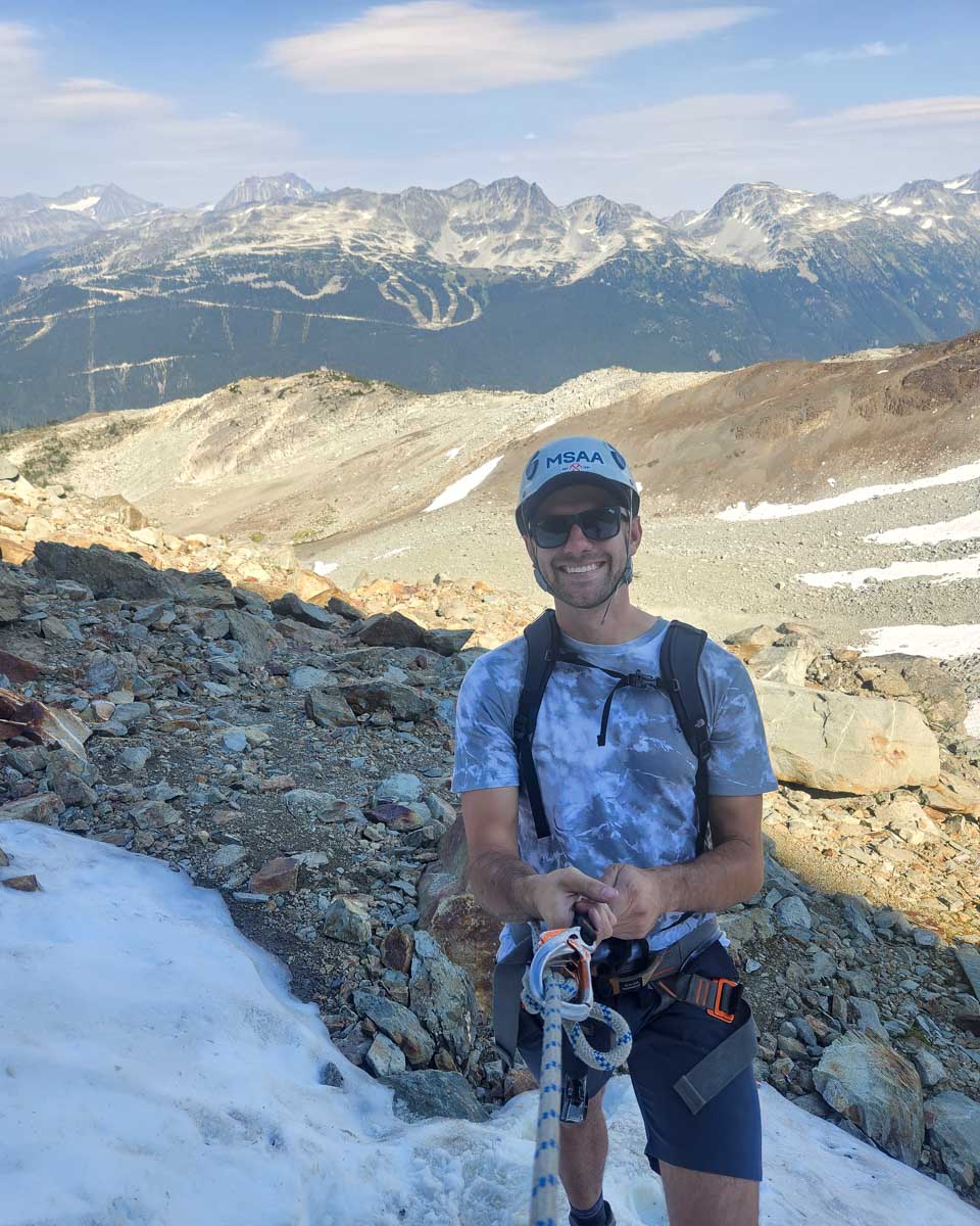 Daniel hanging onto a rope in his gear smiling during Via Ferrata, Whistler, Canada