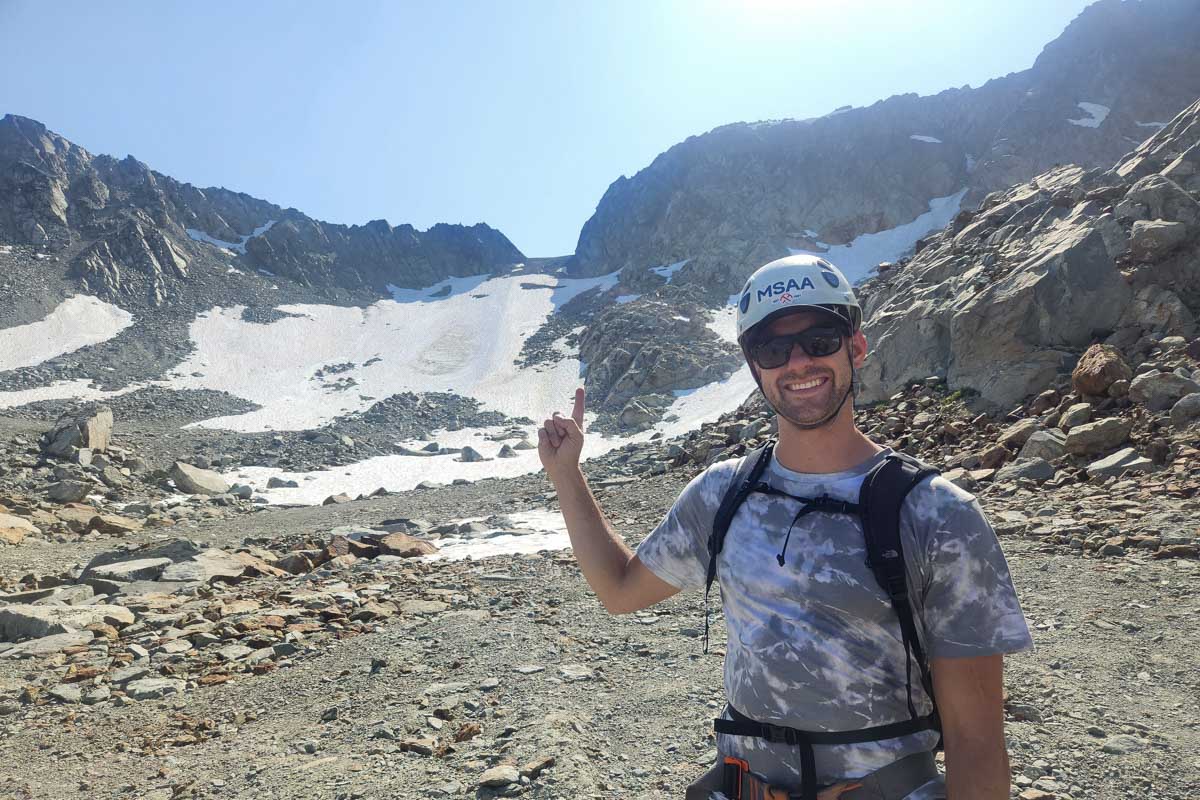 Daniel pointing at whistler behind him and smiling during Via Ferrata, Whistler, Canada