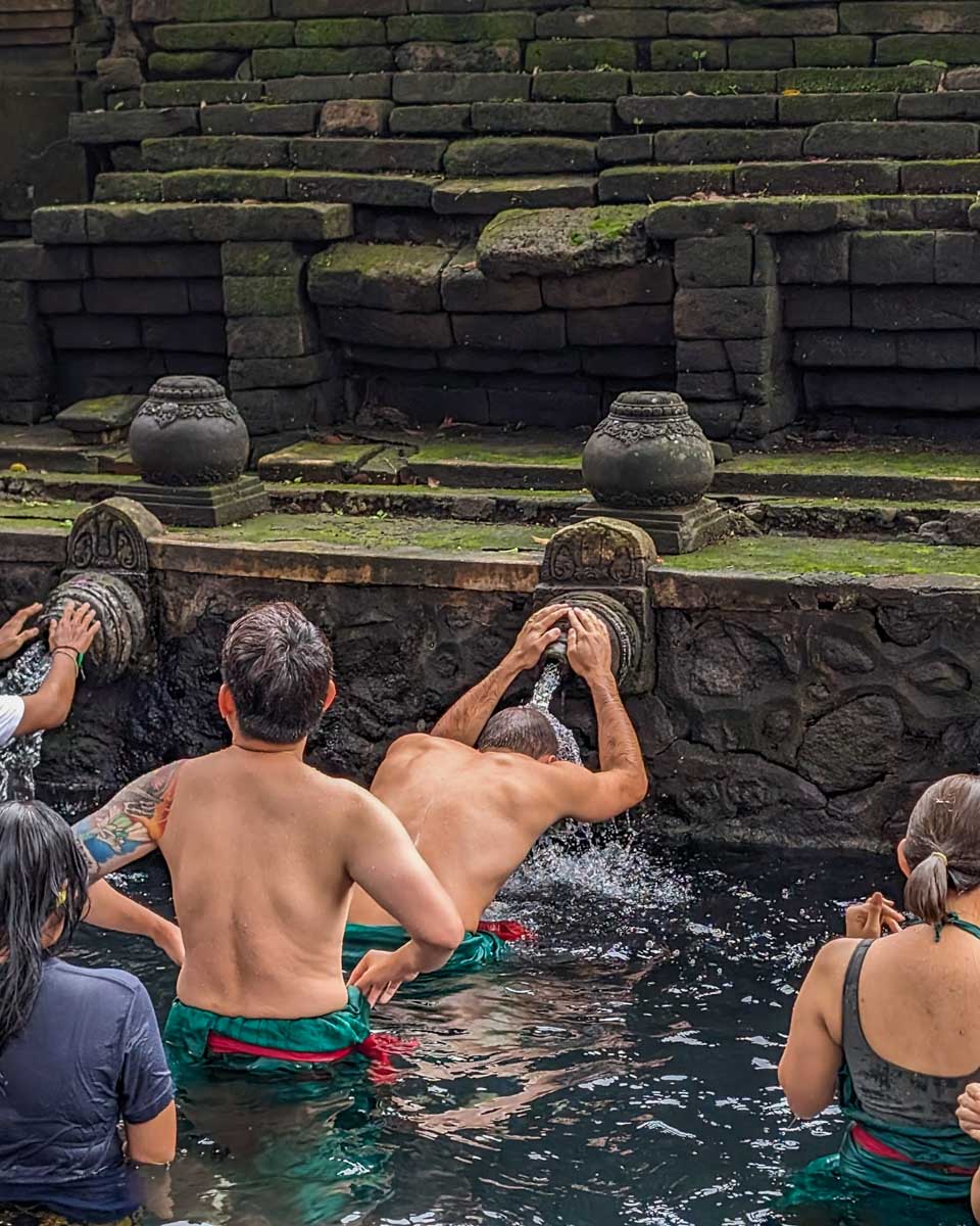 Daniel puts his head under the water at Pura Tirta Empul Temple in Ubud, Bali
