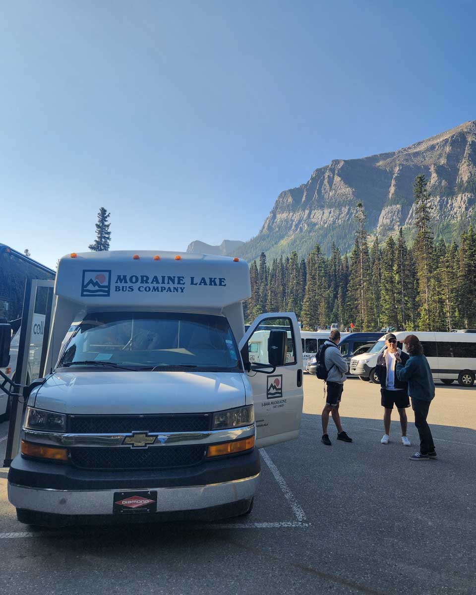 The Moraine Lake Bus Company Shuttle witht mountains behind it Moraine Lake Canada