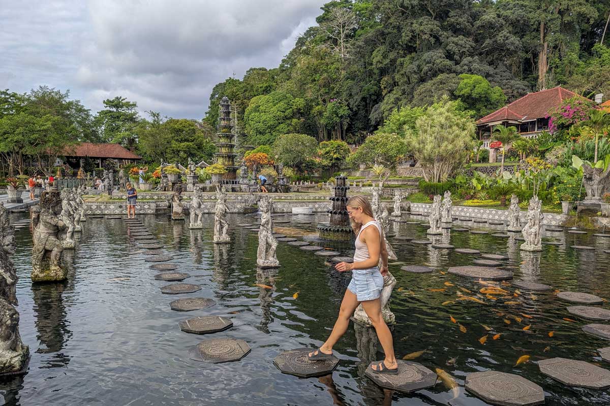 Bailey crosses the pond at tirta gangga on stones with koi fish around during the instagram tour bali
