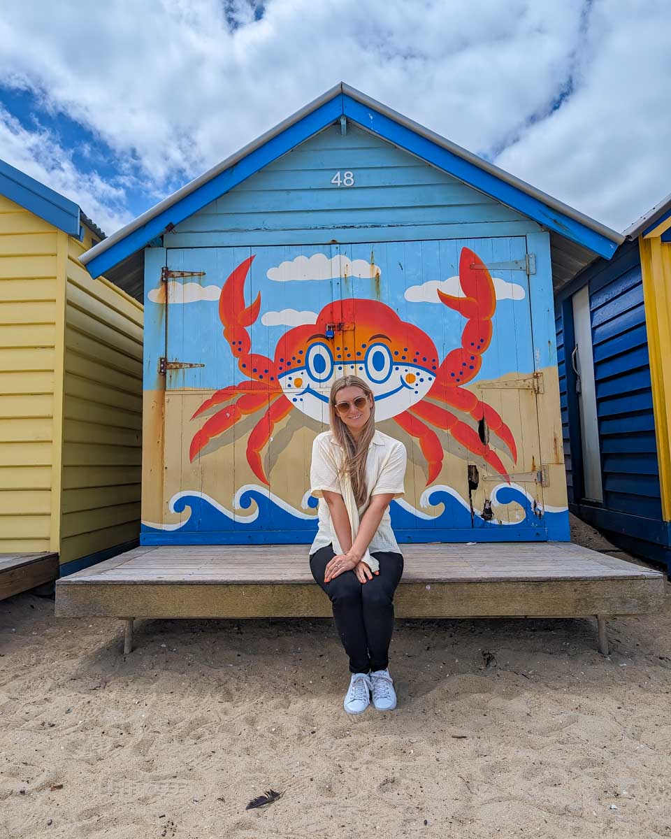 Bailey sits in front of a brighton bathing box with a crab on it during a go west penguin tour to phillip island near melbourne australia