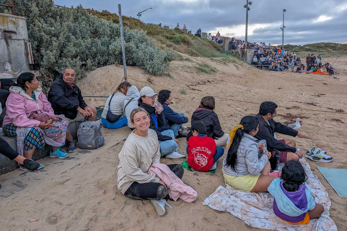 Bailey sits on the beach of penguin watchout on phillip island with other people on a go west penguin tour near melbourne australia