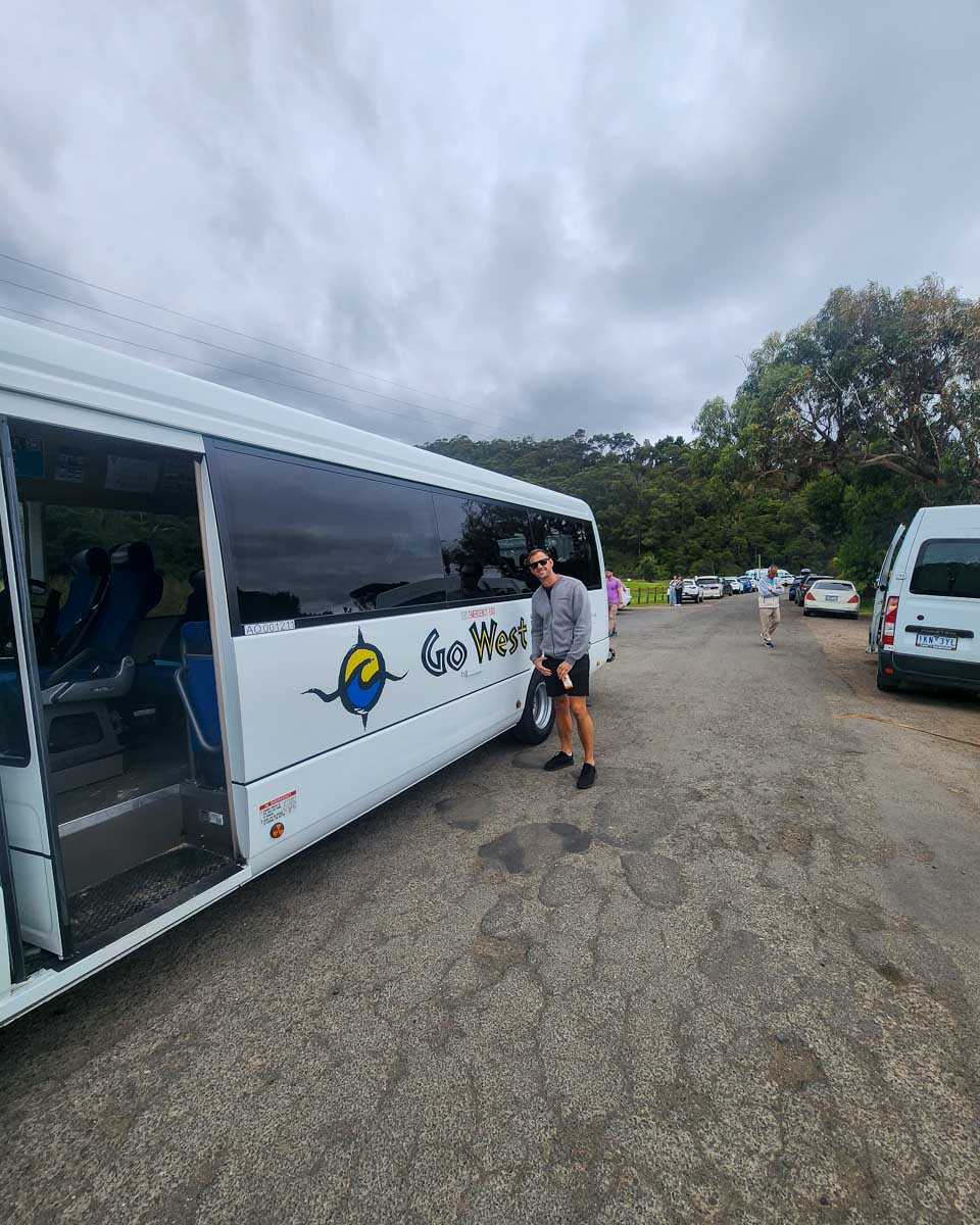 Daniel standing next to a tour bus that says Go West for a great ocean road tour australia
