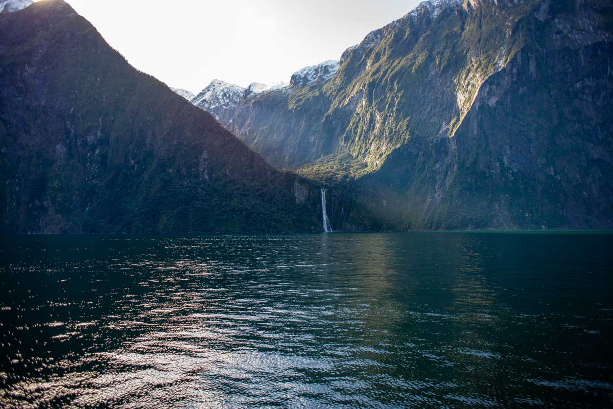 A waterfall far away with sun comingg over the top on the milford sound nature cruise new zealand