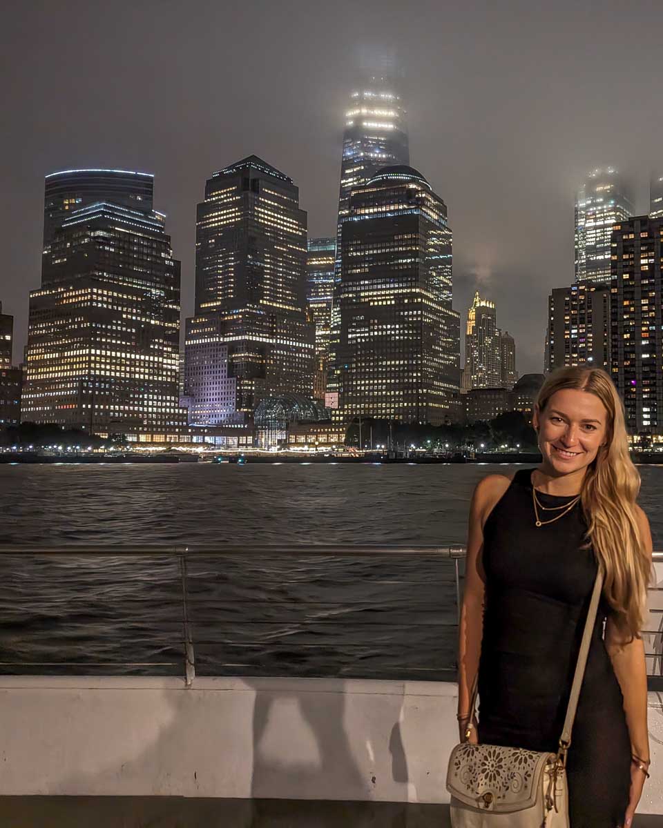 Bailey-poses-for-a-photo-at-night-on-a-dinner-cruise-in-New-York-City-on-the-front-deck-with-the-city-in-the-background through get your guide