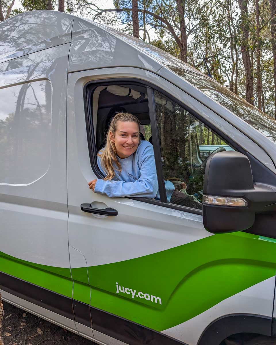 Bailey smiles and leans out of a JUCY campervan while camping in Australia