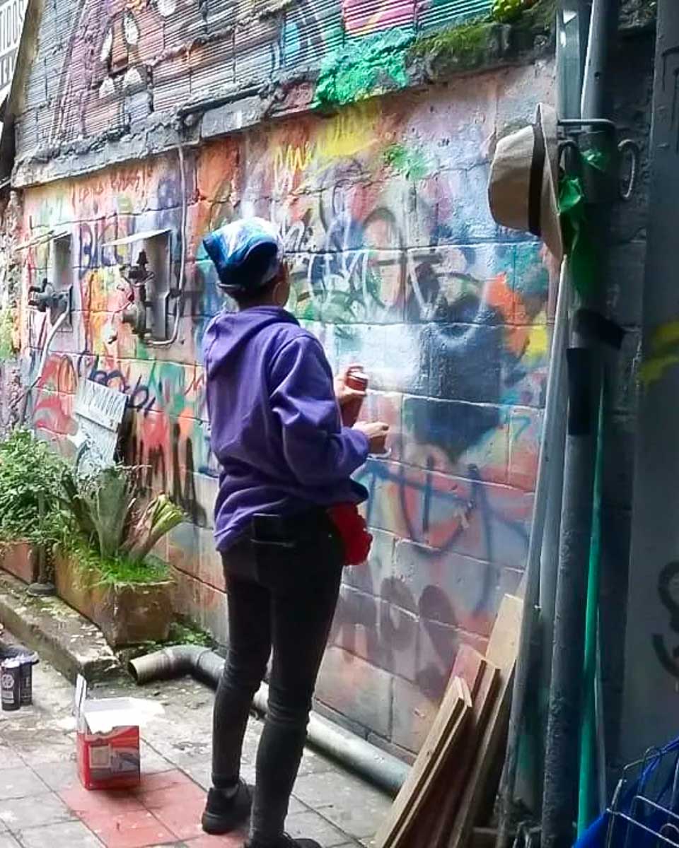 A woman spray paints a wall on a graffiti workshop in Bogota with Capital Graffiti Tours