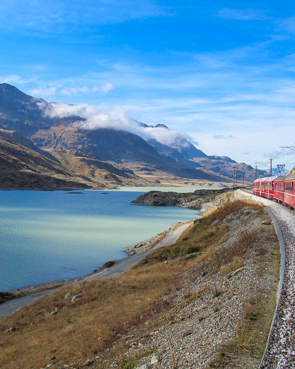 Bernina Express Red Train heading to the Swiss Alps past a lake on a tour from Milan Italy