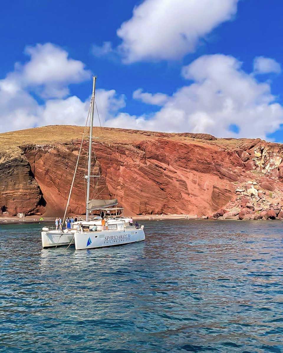 A catamaran in front of the Santorini coastline on a private tour from Santorini Greece