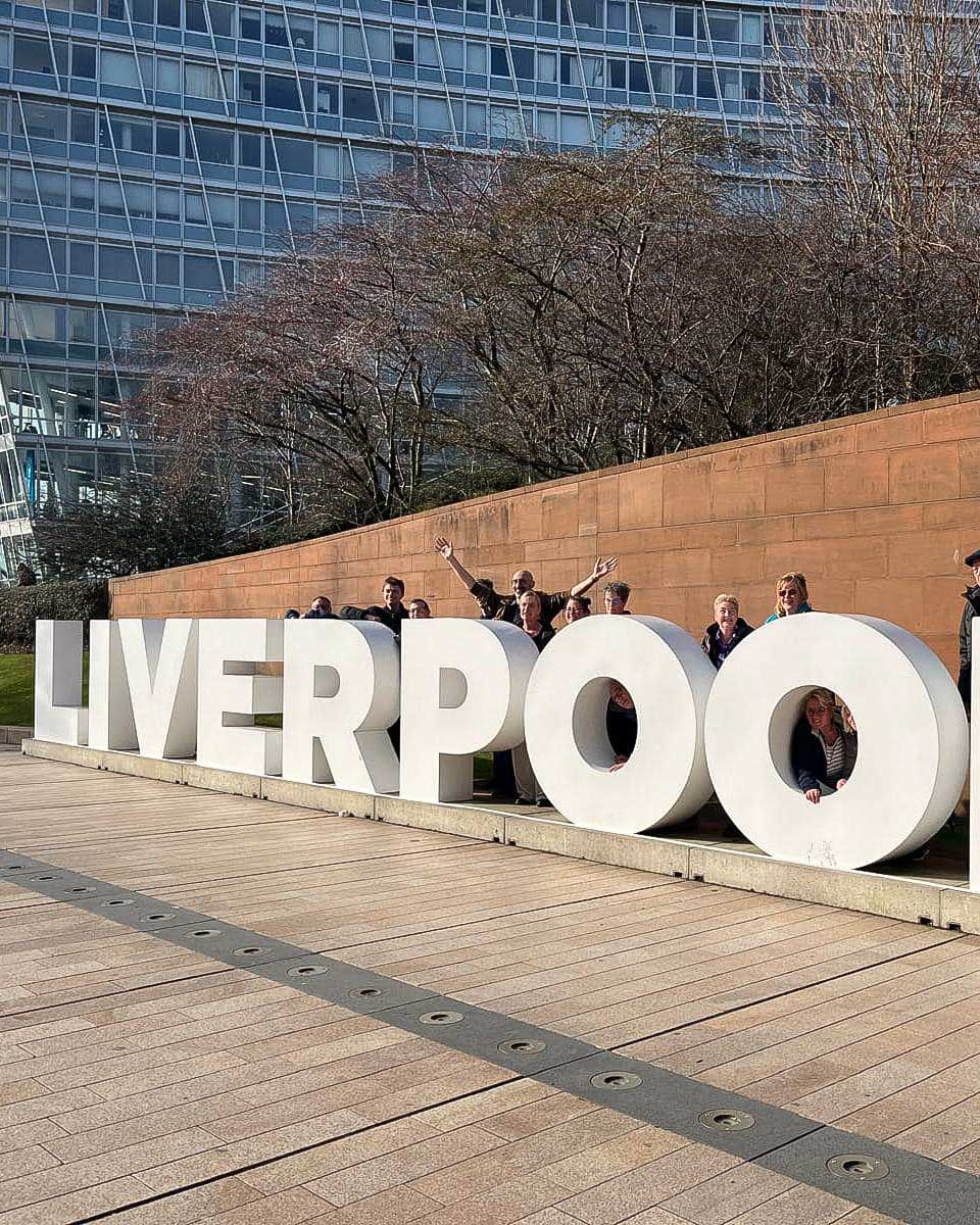 People pose with the Liverpool sign on a walking tour in Liverpool UK